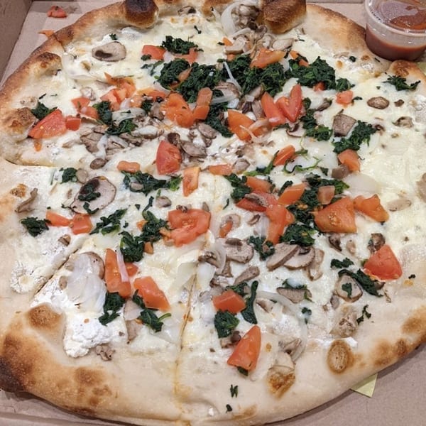 A Niki's Pizza & Pasta white pizza with spinach, tomatoes, mushrooms, and onions.