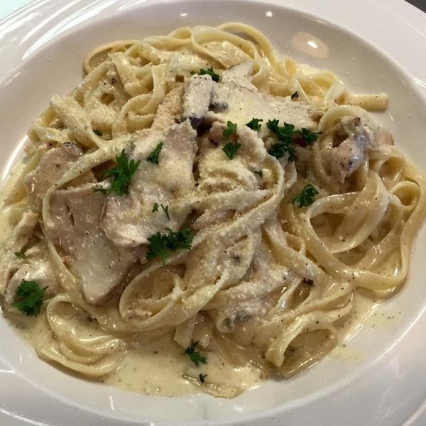 Creamy fettuccine pasta with chicken, parmesan cheese, and parsley in a white bowl.