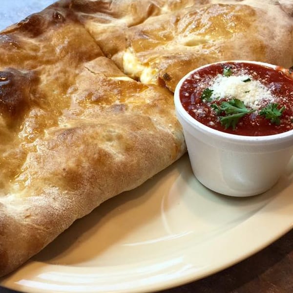 Golden-brown calzone with melted cheese and a side of marinara sauce topped with parmesan and parsley.