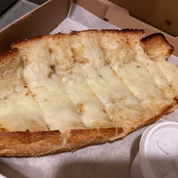 Cheesy garlic bread from Niki's Pizza & Pasta, with melted mozzarella and a side of sauce.