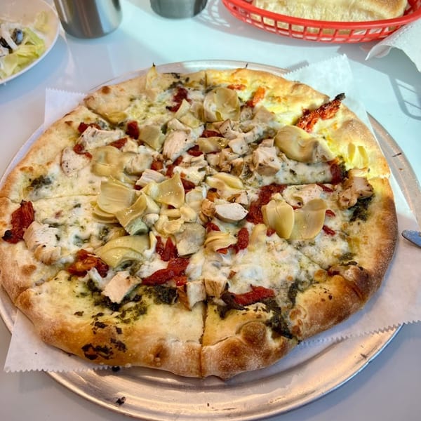 Niki's Pizza & Pasta's chicken, artichoke, and sun-dried tomato pizza on a metal tray.