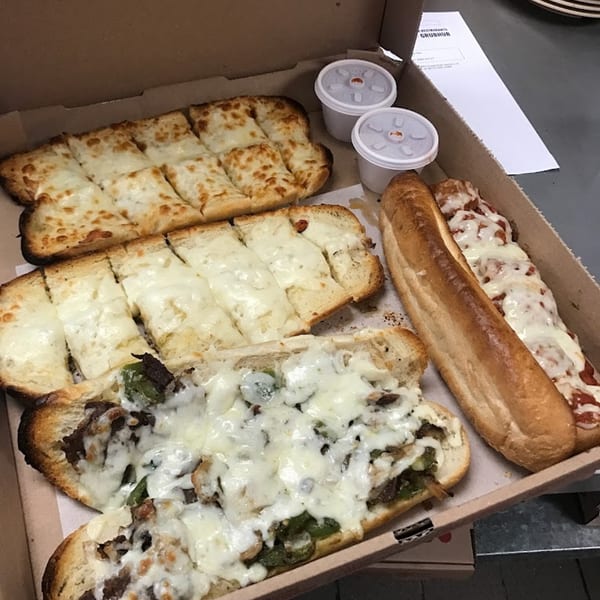 A Niki's Pizza & Pasta box with cheesy bread, a meatball sub, and a cheesesteak sub.